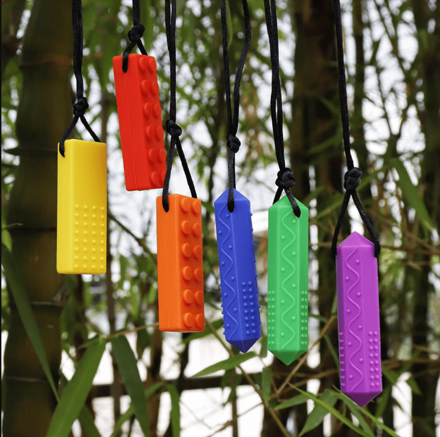 Five Colorful Sensory Chewable Necklaces Hanging In Front Of Greenery