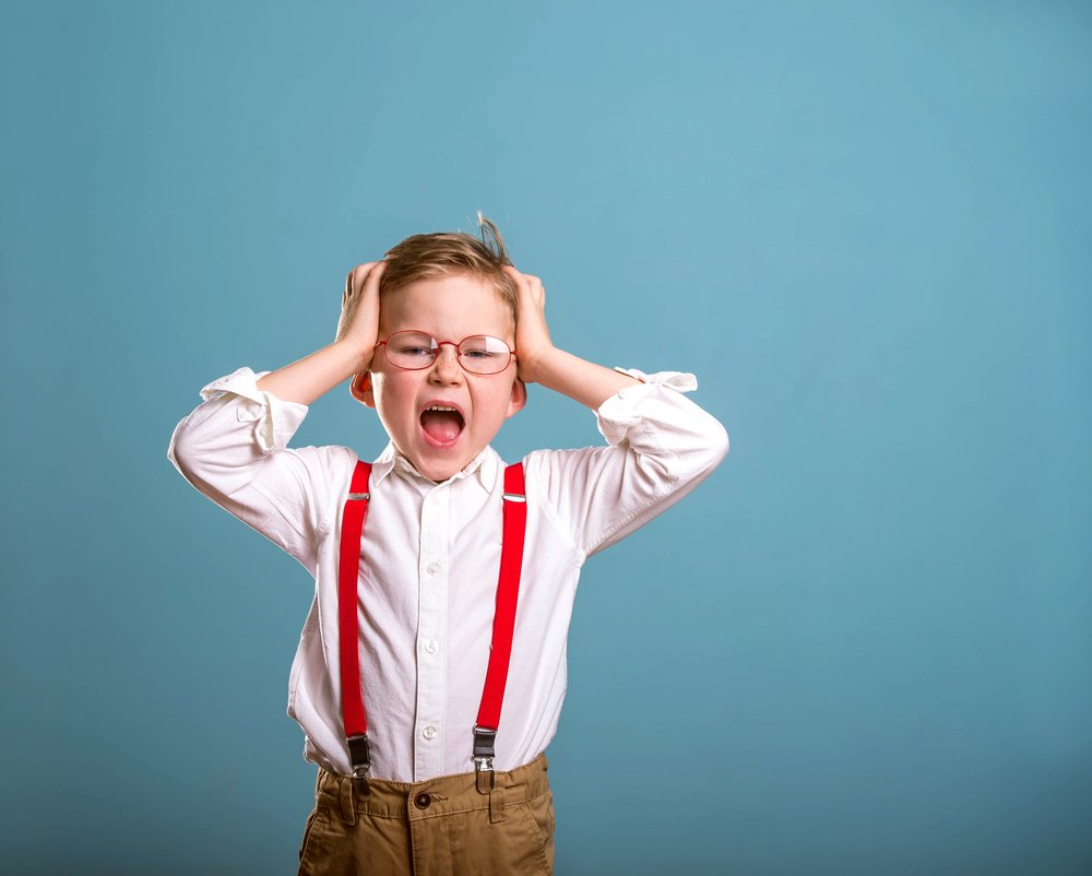 Little Boy In Suspenders Screaming And Throwing Tantrum With Blue Backdrop