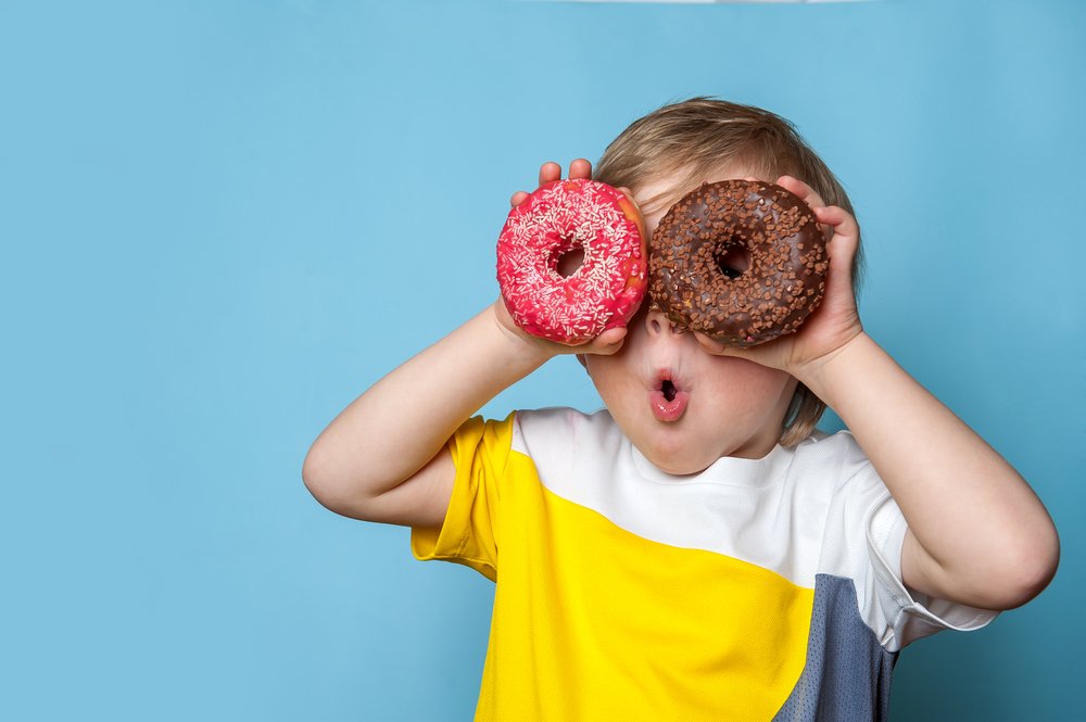 Toddler Holding Two Donuts Up In Front of His Eyes