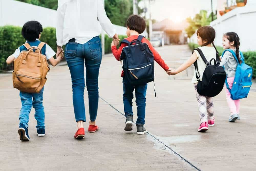 A Mother Walking Her Children Into Daycare Wearing Backpacks and Holding Hands