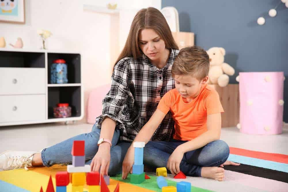 Woman Playing Wooden Blocks With A Child In Daycare