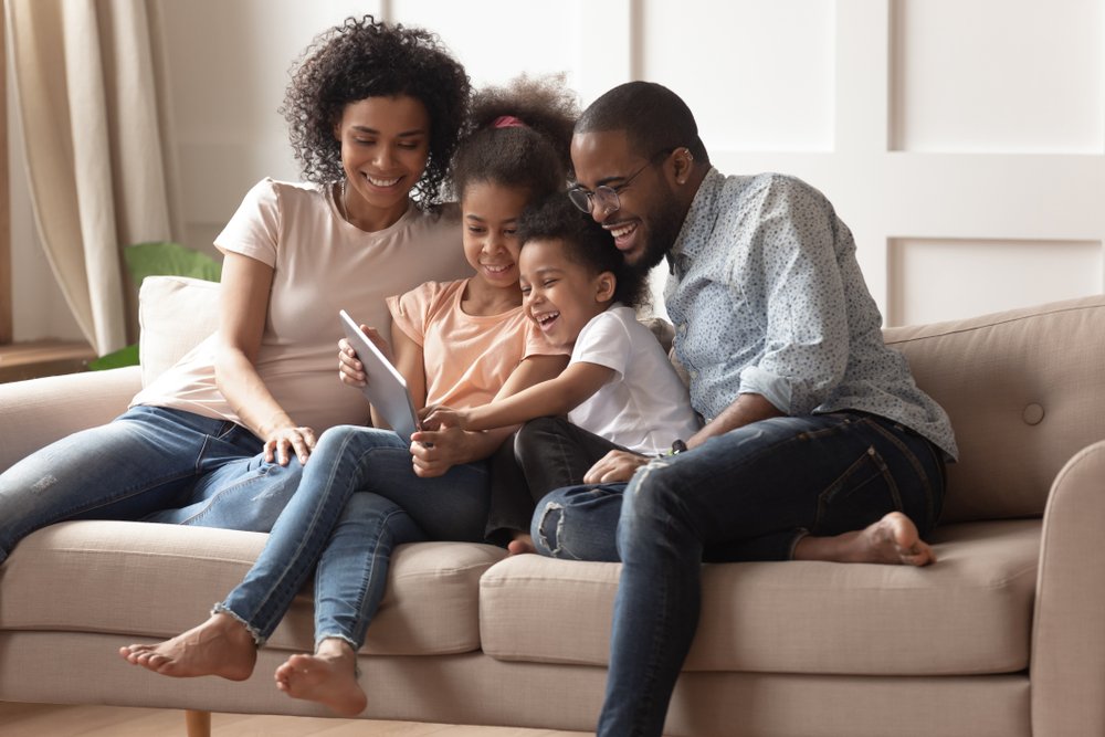 Mother And Father Reading On A Couch To Their Two Children Between Them