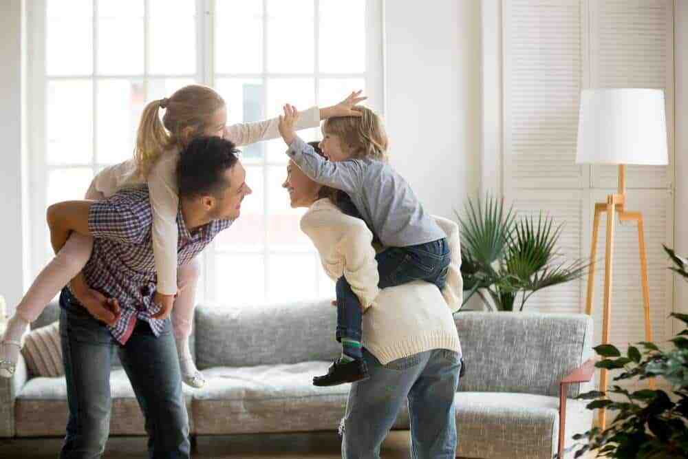 Mother and Father Giving Their Children Piggyback Rides In A Living Room