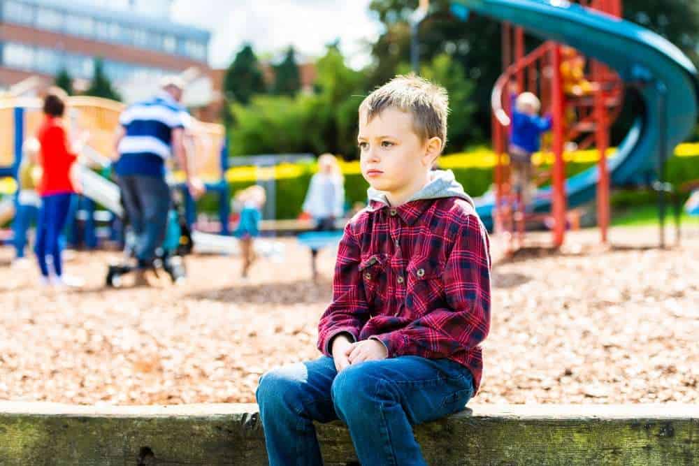 Young Boy With Autism Sitting By Himself At The Edge of the Playground 