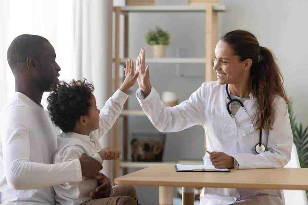 Female Doctor Giving A Young Boy With Autism A High-Five While His Dad Holds Him