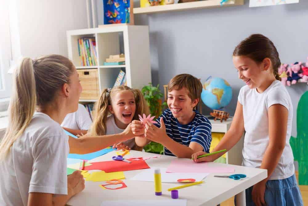 Four Kids Laughing Around A White Table Full Of Crafts and Games