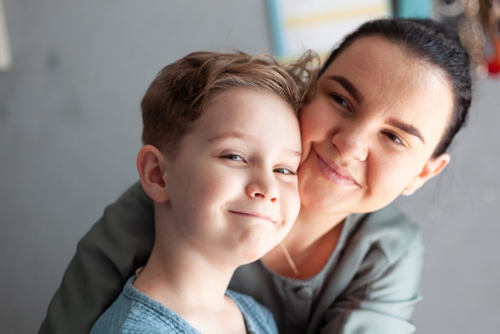 Child With Autism Smiling And Being Hugged By His Mother