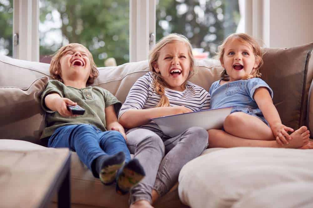 Three Siblings Sitting On A Couch & Laughing