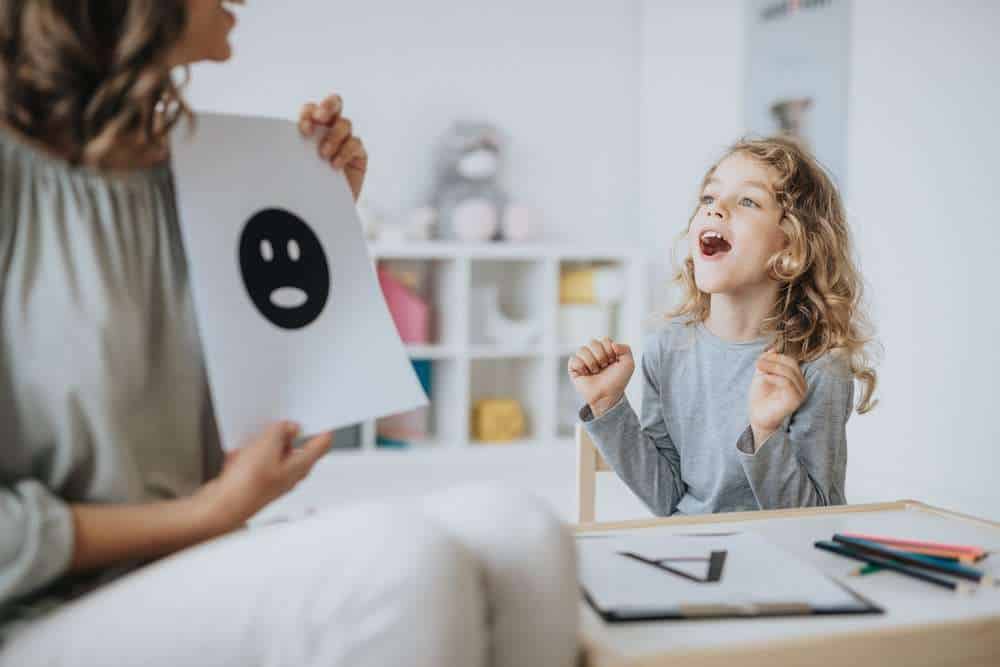 Young Girl With Autism At ABA Therapy  Where The Therapist Is Holding An Image of A Face