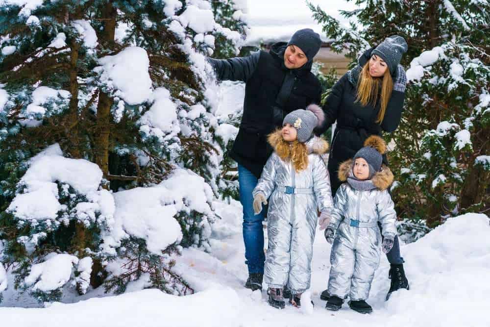 Two Parents Outside In Snow With Their Two Kids Looking At Trees