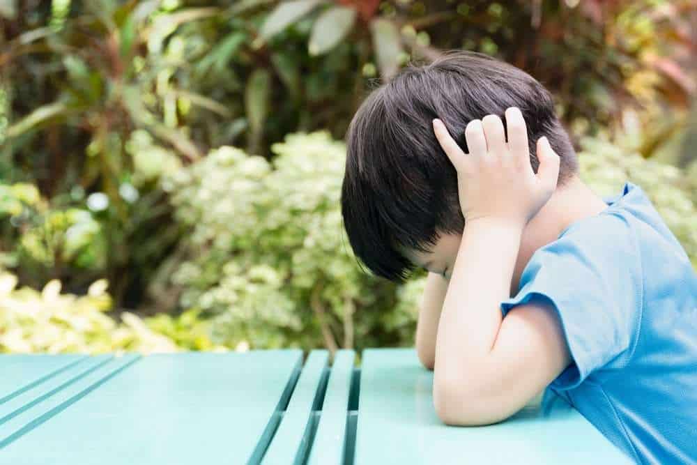 Boy With Autism Sitting At Picnic Table And Covering Ears To Self Stimulate