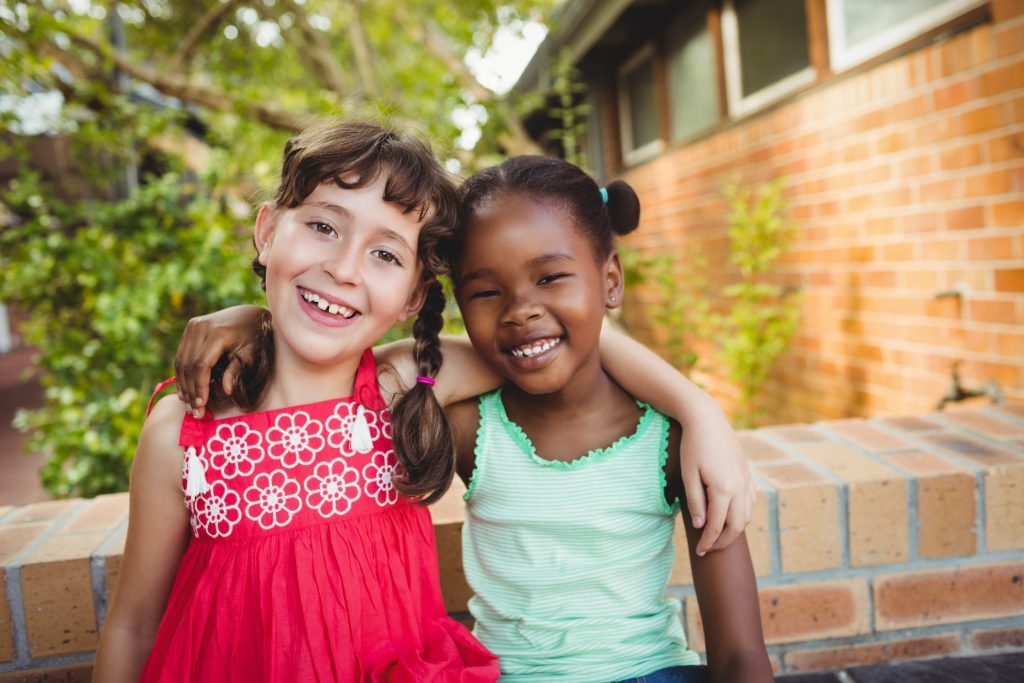 Two Young Girls Hugging And Smiling At The Camera