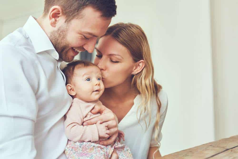 Two Parents Holding Infant Daughter and Kissing Her Head