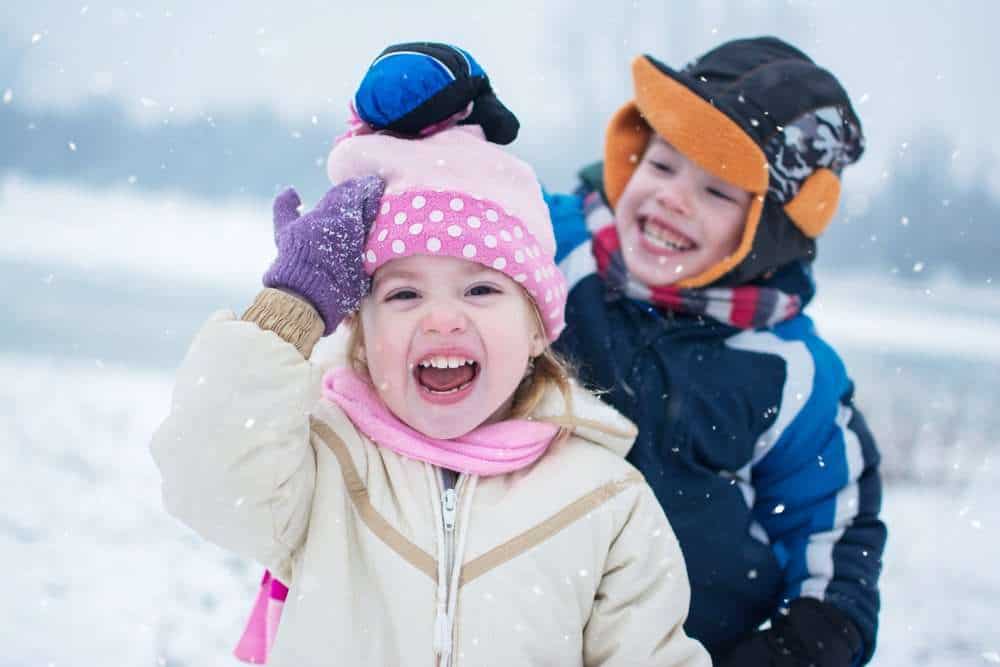 Cheerful Siblings In Winter Outfits Playing Together On A Snowy Day