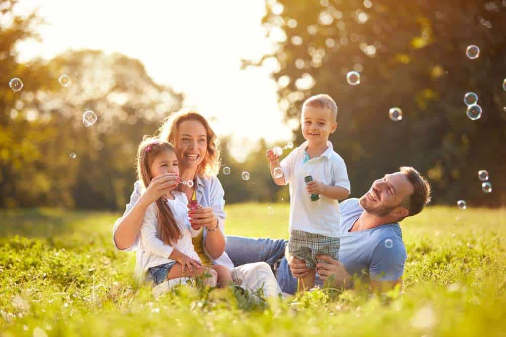 Family Of Four Blowing Bubbles In A Field